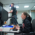 Female student analyzing data while a male student runs on a treadmill to the side of her.