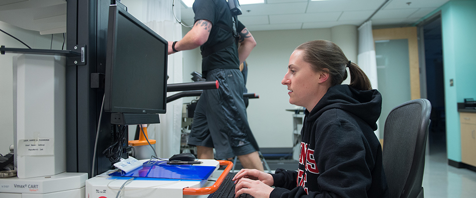 Female student analyzing data while a male student runs on a treadmill to the side of her.