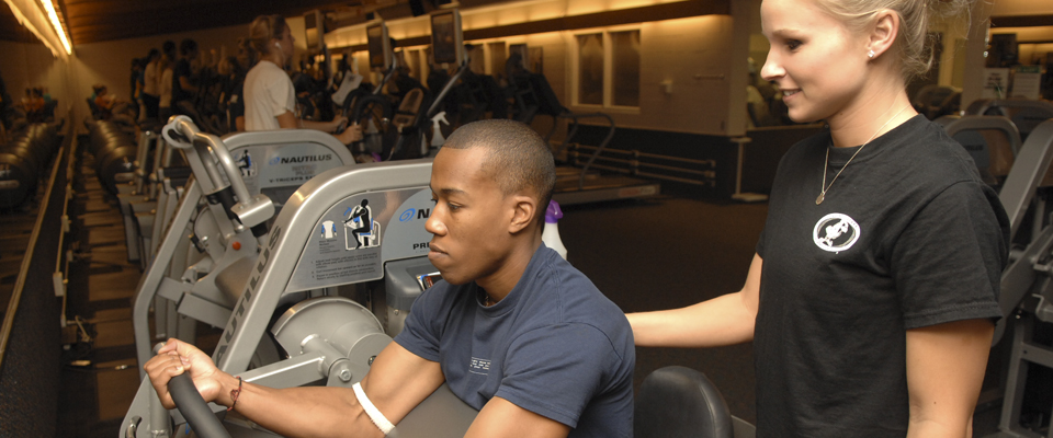 A biomechanics graduate student analyzing another student's movement on a weight machine.